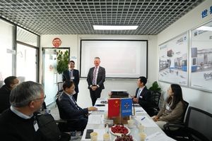 Mr. Franz Roessler, Commercial Counsellor of the Austrian Embassy in China (right), delivering the welcoming speech, with Mr. Jin Yaohua, Senior Marketing Officer, providing on-site translation (left). A boardroom with two presenters and a couple of people listening to them